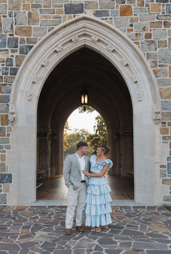 couple standing together in front of historic berry college archway while wearing a blue dress and gray suit