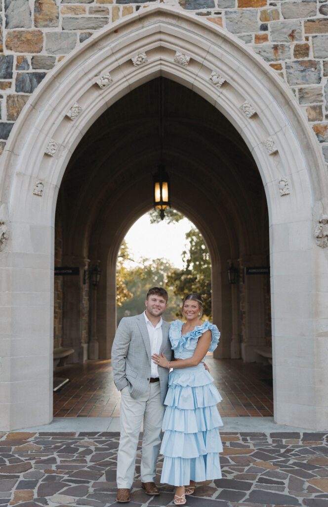 couple standing in front of the archway at berry college while smiling at the camera
