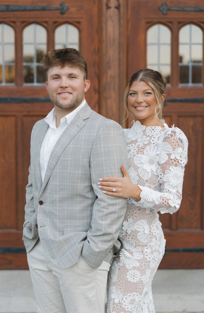 engaged couple standing in front of historic wooden doors at berry college wearing a white lace formal gown