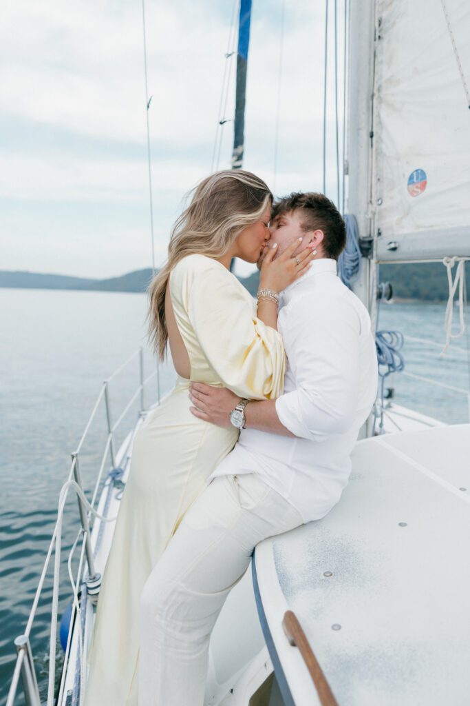 soon to be wife and groom kissing on the side of the sailboat during engagement session