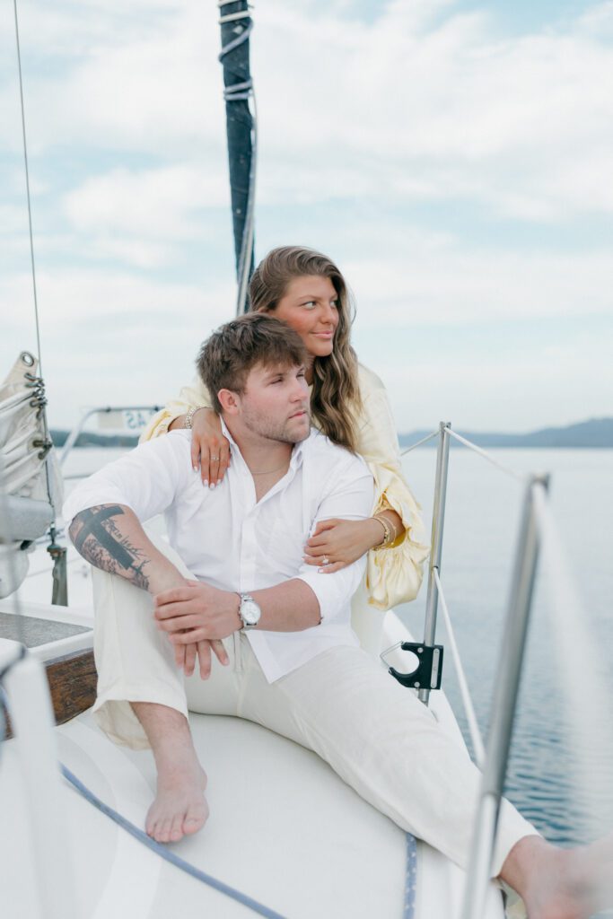 engaged couple looking out on the lake while sitting on a sailboat and enjoying the breeze