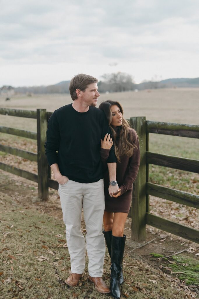 Woman leaning on her fiance's arm while standing by the wooden fence at Pursell Farms for her engagement photos